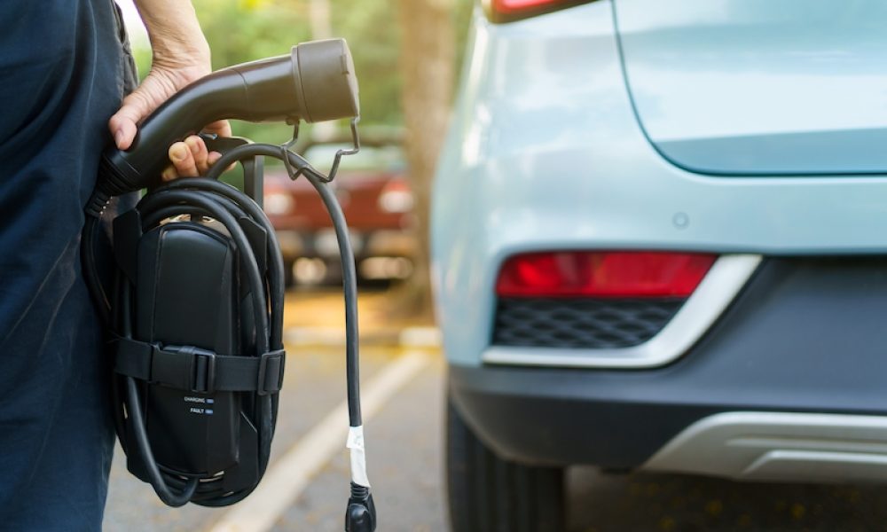 Unrecognizable woman holding the portable EV emergency charging adapter and preparing to charge the EV car. Electric Vehicle charging adapter close up with copyspace.